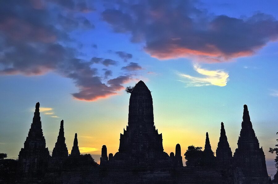 Wat Chaiwatthanaram silhouetted against a glowing sky at sunset in Ayutthaya